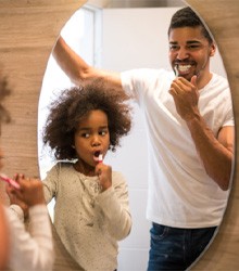 Father and daughter looking in mirror while toothbrushing in Wellesley 