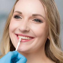 Cosmetic dentist holding up a color guide to a smiling woman who just got teeth whitening  