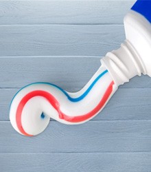 Closeup of a tube of toothpaste spilling out a swirl of white toothpaste with red and blue stripes
