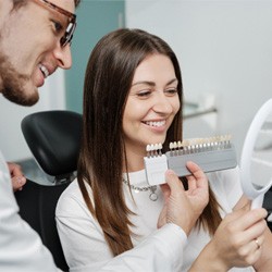 Wellesley cosmetic dentist holding a mirror up for a smiling patient 