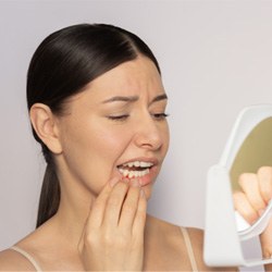 Concerned woman touching her cheek, gums, and jawbone and looking into the mirror