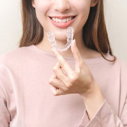 Smiling woman holding Invisalign clear aligner