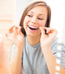 Woman looking at herself in a mirror while flossing in Wellesley