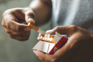 Man pulling cigarette from carton, preparing to smoke