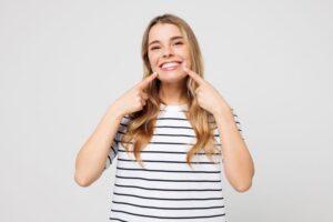 Woman with straight teeth pointing at her smile 